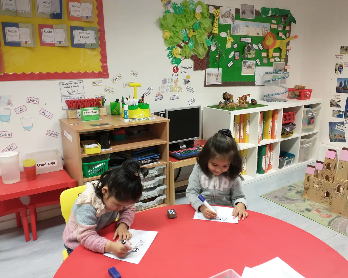 Two children practising writing their names at a table in an Iqra Preschool classroom