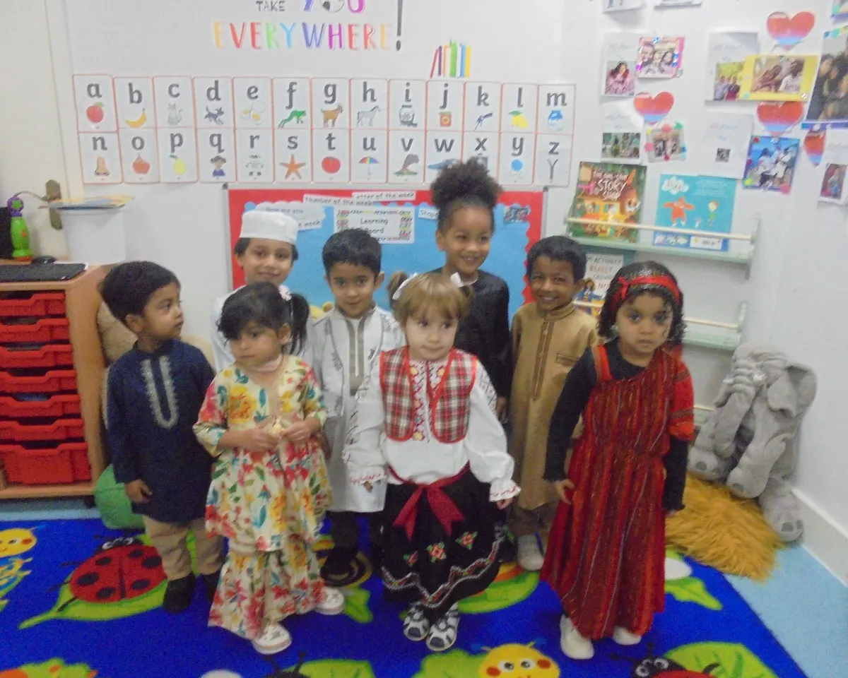 Children at Iqra Preschool dressed in traditional clothes from around the world, smiling in front of the alphabet wall