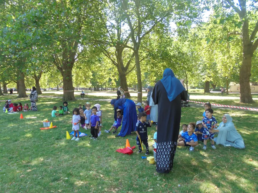 Children playing outdoor games in the park with Iqra Preschool staff on a sunny day